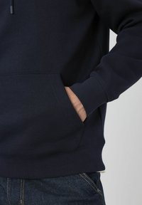 Sweat-shirt marine avec capuche à cordon de serrage, poche kangourou, poignets et ourlet côtelés. Tissu doux et texturé ; un jean coordonné est visible en dessous.