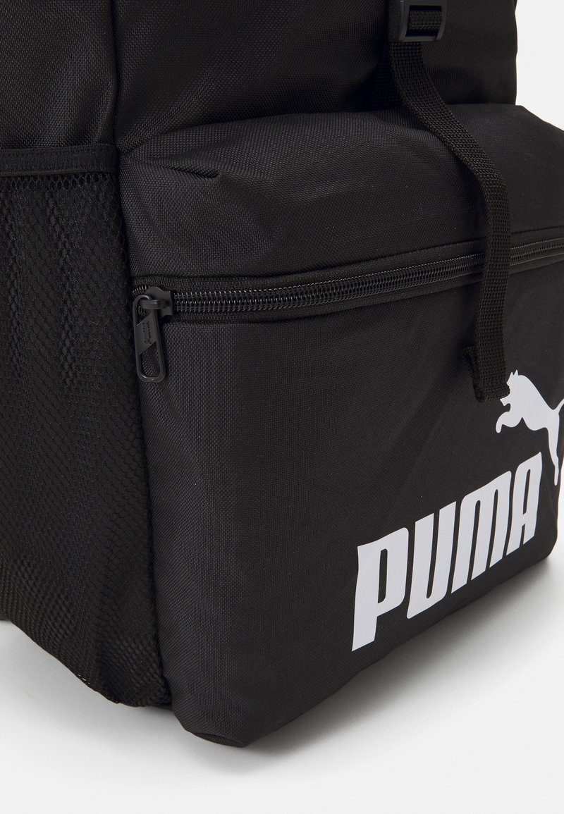 Zaino nero con tessuto texturizzato, dotato di un compartimento con cerniera, tasca laterale in rete e un grande logo Puma bianco sulla parte anteriore.