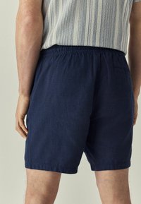 Mørkeblå shorts lavet af tekstureret stof, med elastisk talje og en baglomme. Flade kantede kanter uden yderligere accenter.