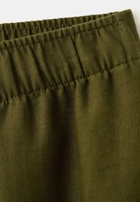 Détail de la ceinture élastique sur un tissu tissé vert olive, montrant des fronces et la texture.