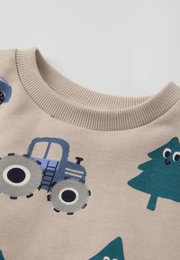 Beige katoenen sweater met graphics van een blauwe tractor en een groene boom, met geribbelde ronde hals en een gladde textuur.