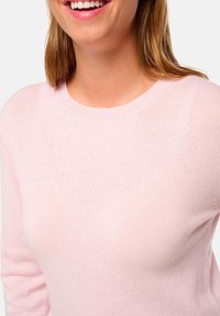 Pull en maille rose clair avec un col rond et des manches longues, présentant une texture douce et une coupe ajustée.