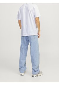 Camiseta blanca de algodón, de manga corta, ajuste relajado, combinada con jeans holgados de color azul claro. El calzado presenta acentos en gris y negro.
