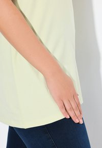 Licht gele katoenen T-shirt met een afgeronde zoom, gecombineerd met donkerblauwe denim. De textuur is glad, met korte mouwen en minimale naden.