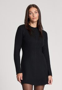 Vestito nero a coste in maglina con maniche lunghe, corpino aderente e gonna a ruota. Presenta una texture verticale e un collo rotondo.