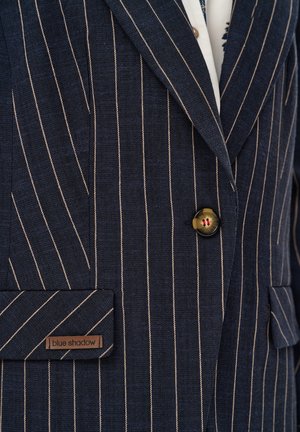 Granatowa marynarka w prążki z pojedynczym zapięciem na guzik, klapą z wycięciem, przednią kieszenią z patką oraz metką "blue shadow" na patce kieszeni.
