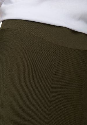 Olijfgroene geribbelde rok met een rekbare textuur en een gladde tailleband, gedeeltelijk bedekt door een wit topje.