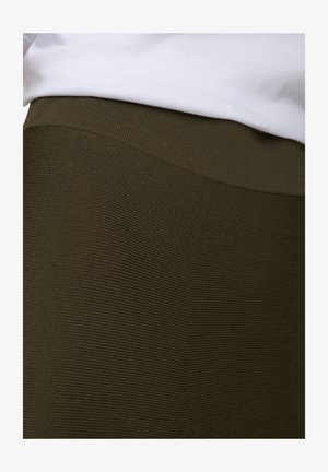 Olijfgroene geribbelde rok met een rekbare textuur en een gladde tailleband, gedeeltelijk bedekt door een wit topje.