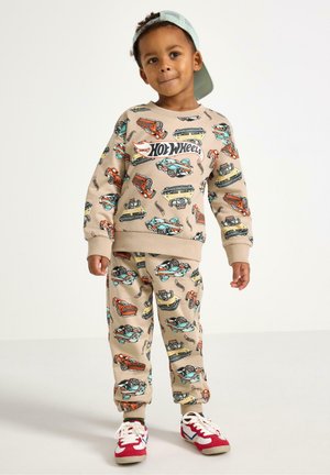 Beige sweatshirt en broek met kleurrijke autopatronen, voorzien van ribgebreide manchetten en tailleband. Rode en witte sneakers maken de outfit compleet.