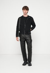 Melna džinsa jaka ar rāvējslēdzēja aizdari un sānu kabatām, kombinēta ar melnām ādas cargo biksēm, kurās ir vairākas kabatas un stilīgs dizains.