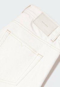 Gros plan sur un jean en denim blanc montrant la poche arrière et un patch rectangulaire marqué MNG DENIM sur la ceinture.