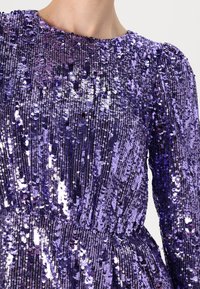 Vestido roxo de lantejoulas com decote redondo e mangas bufantes, apresentando uma superfície brilhante e texturizada com linhas verticais de lantejoulas.