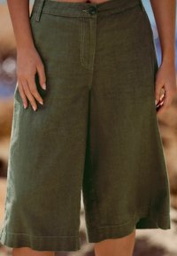 Olivově zelené lněné kalhoty culottes se širokou nohavicí, na knoflíkové zapínání, s předními švy a středním pasem. Texturovaná látka, volný střih.