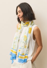 Lekki, przezroczysty szal z wzorem cytrynowych kwiatów, głównie biały z niebieskimi i żółtymi akcentami. Miękka tekstura z frędzlami na brzegach.