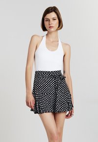 Costume da bagno bianco con collo halter abbinato a una gonna avvolgente nera a pois con volant. Tessuto liscio, lunghezza corta e accentuazione con fiocco in vita.