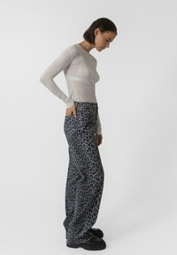 Top trasparente a maniche lunghe di colore grigio chiaro, abbinato a jeans grigi dalla vestibilità ampia con stampa leopardata nera. Tessuto testurizzato e silhouette morbida.