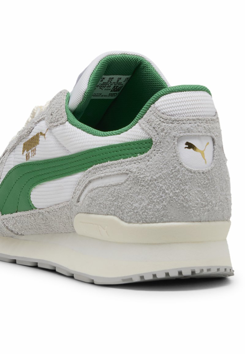 Zapatilla verde y blanca con un talón de gamuza gris texturizada, logo dorado y una suela blanca acolchada. Presenta materiales de malla y sintéticos.