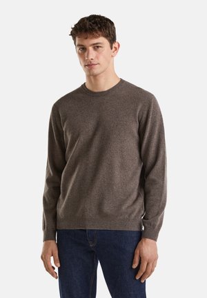 Maglione marrone lavorato a maglia con scollo rotondo e maniche lunghe. Tessuto morbido, polsini e orlo a coste, abbinato a jeans blu scuro.