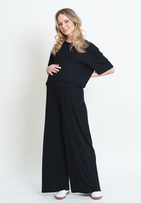 Top corto nero con maniche corte larghe e pantaloni neri a vita alta, fluidi. Tessuto morbido, vestibilità rilassata. Sneakers bianche completano l'outfit.