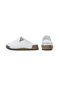 Witte slippertjes met een matte afwerking, voorzien van een metalen logo-detail, een gestructureerde bruine zool en een open achterkant.