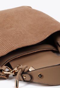Una borsa a tracolla in corduroy color beige parzialmente aperta, che rivela un interno liscio e una catena dorata attaccata alla tracolla. Design pulito e moderno.