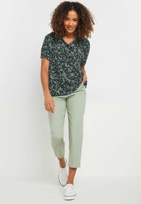 Blusa negra con flores, de mangas cortas y escote en V, combinada con pantalones verdes claros ajustados y zapatillas blancas.
