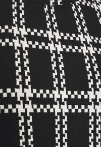 Tissu noir avec un motif à carreaux blancs composé de petites formes carrées créant un dessin en grille.