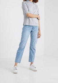 Light gray, lightweight hoodie with a relaxed fit and three-quarter sleeves, paired with light blue straight-leg jeans and white sneakers.