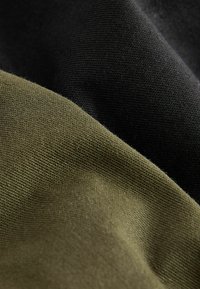 Deux échantillons de tissu : l'un vert olive avec une texture douce et l'autre noir avec une finition lisse, tous deux d'apparence mate.