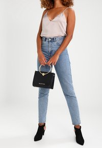 Ljusgrå satinspets med tunna axelband, högmidjade blå jeans, svart handväska med guldringshandtag och svarta ankelskor.