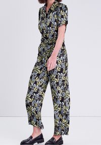 Combinaison à motifs floraux avec des manches courtes, taille cintrée et pantalons fluides dans des tons de noir, vert et bleu ; texture de tissu lisse.