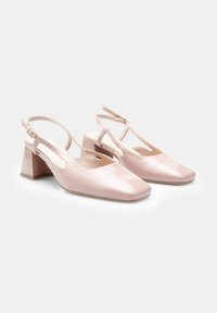 Pink patent leather slingback shoes with a square toe and low block heel; features a buckle strap and cut-out design.