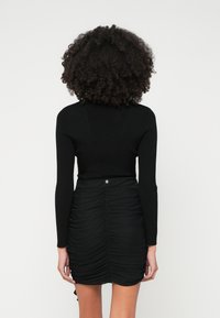 Μαύρη ριμπ μπλούζα με μακριά μανίκια σε συνδυασμό με εφαρμοστό μαύρο πλισέ φούστα, η οποία διαθέτει ασημί λεπτομέρεια στη μέση. Λείο υλικό σε όλη την επιφάνεια.