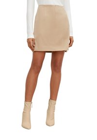 Mini-jupe beige à texture lisse, coupe ajustée et fermeture éclair au dos. Associée à des bottines beige ajustées montant à la cheville.