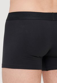 Schwarze Bio-Baumwoll-Boxershorts mit einem weichen Bund, der das prägnante Branding "OrganicBasics" trägt, glatter Textur und enganpassendem Design.