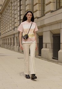 Light pink and orange gradient t-shirt, cream flared pants, and black ankle boots. Small black crossbody bag with gold hardware.