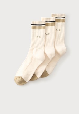 Trois paires de chaussettes côtelées couleur crème avec des accents beiges aux orteils et au talon, ainsi qu'une bande beige et noire près du haut.