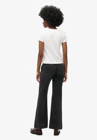 Pantalones vaqueros anchos negros de cintura alta, con bolsillos traseros y dobladillo sin rematar. Combinados con una camiseta ajustada blanca de manga corta.