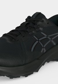 Μαύρο αθλητικό παπούτσι Asics με υφασμένο πέλμα, κορδόνια μπροστά και γκρι ρίγες λογότυπου στο πλάι.