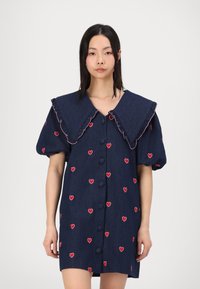 Ναυτικό φόρεμα από τζην με υπερμεγέθη φουσκωτό γιακά, φουσκωτά μανίκια και κέντημα κόκκινης καρδιάς. Διαθέτει κλείσιμο με κουμπιά μπροστά και υφή υφάσματος.