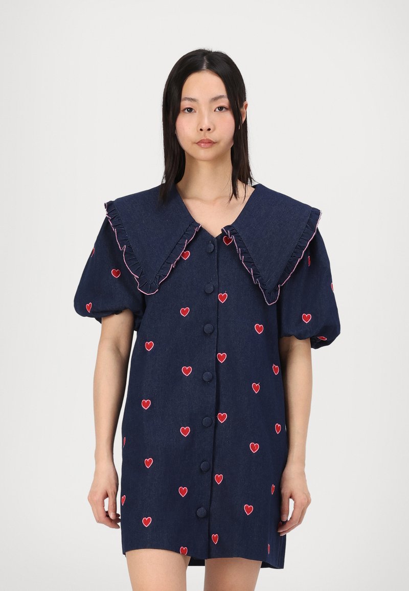 Ναυτικό φόρεμα από τζην με υπερμεγέθη φουσκωτό γιακά, φουσκωτά μανίκια και κέντημα κόκκινης καρδιάς. Διαθέτει κλείσιμο με κουμπιά μπροστά και υφή υφάσματος.