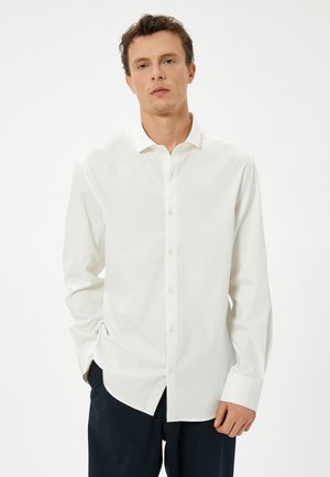 Camisa blanca de manga larga tipo button-up con cuello, con una textura suave y dobladillo recto, combinada con pantalones oscuros.