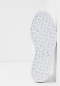 Bílá podrážka tenisky s texturovaným vzorem malých trojúhelníků, která obsahuje detail loga. Materiál vypadá gumově a hladce.