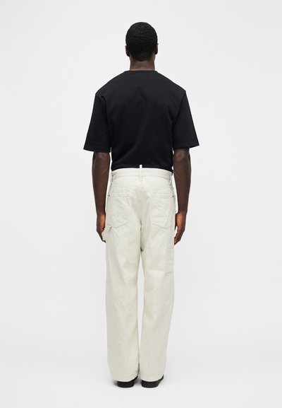 Camiseta negra de manga corta combinada con pantalones cargo de corte holgado en beige claro, con dos bolsillos traseros y textura suave.