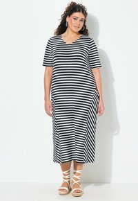 Wzorzysta, granatowo-biała sukienka do kolan z krótkimi rękawami, dekoltem w serek i bocznymi kieszeniami, zestawiona z białymi sandałami na paski.