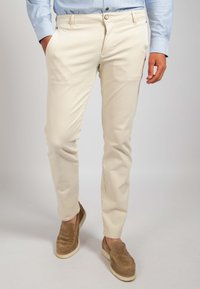 Beige Baumwollhosen mit schlanker Passform, ausgestattet mit Fronttaschen und einer glatten Textur, kombiniert mit braunen Wildleder-Schlupfschuhen.