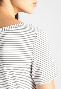 Biała i szara paskowana koszula z krótkim rękawem i okrągłym dekoltem, charakteryzująca się gładką, bawełnianą teksturą i luźnym krojem.