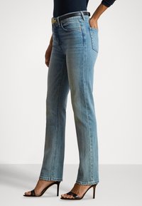 Gaiši zili džinsa džinsi ar taisnu kāju griezumu, augstu vidukli un smalku izbalējumu. Kombinēti ar melnām sandaletēm ar papēdi un pieguļošu topu.