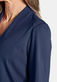 Marineblaues Langarmoberteil mit V-Ausschnitt, weichem Stoff und glatter Textur. Das Design bietet eine lockere Passform und einen leichten Glanz.