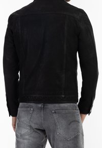 Musta nahkatakki, jossa on sileä pinta, klassinen kaulus ja olkaompeleet, yhdistettynä harmaisiin denim-farkkuihin.